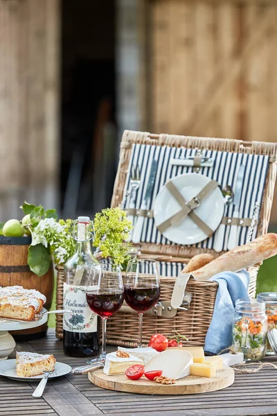 Vintage picnic hamper with wine, bread, cheese platter and freshly baked tart for dessert on a table in the garden