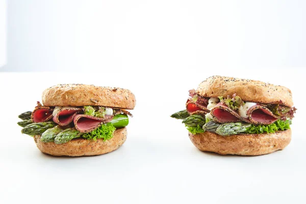 Two healthy fresh green asparagus burgers with sliced ham and mayonnaise on crusty buns viewed to the side on white with copy space