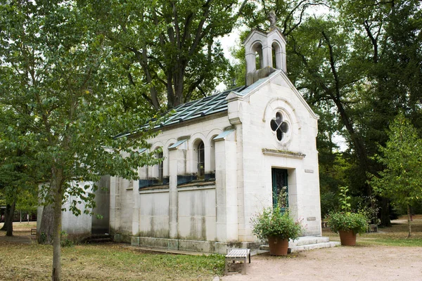 ベンチが置かれた公園内の礼拝堂には庭師が手入れした木に囲まれた花器が飾られています — ストック写真