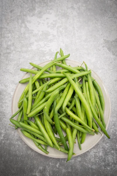 Fresh green string beans on a plate on grey structured background.