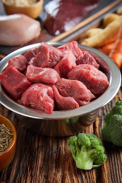Assorted fresh ingredients for healthy dog and cat food with a dish of diced raw beef, chicken, cereal, liver and broccoli on an old rustic wooden floor