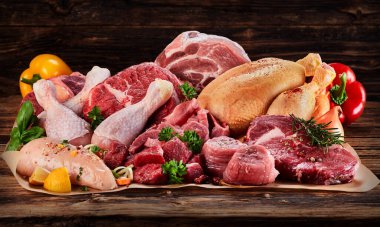Raw meat assortment on cooking paper with greens and vegetables, viewed in close-up on wooden table clipart