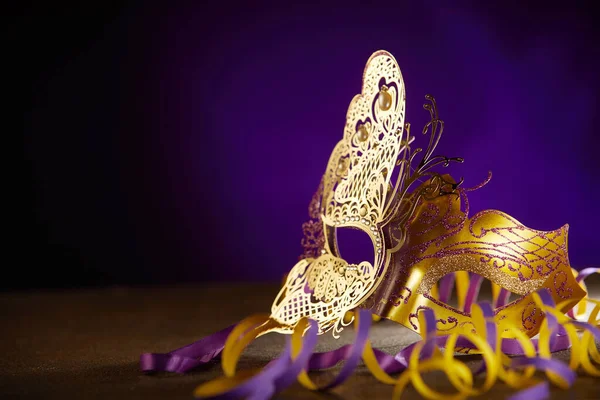 Close up on small metal mask with butterfly engraving lying on the ground next to spiraling ribbons colored purple and orange