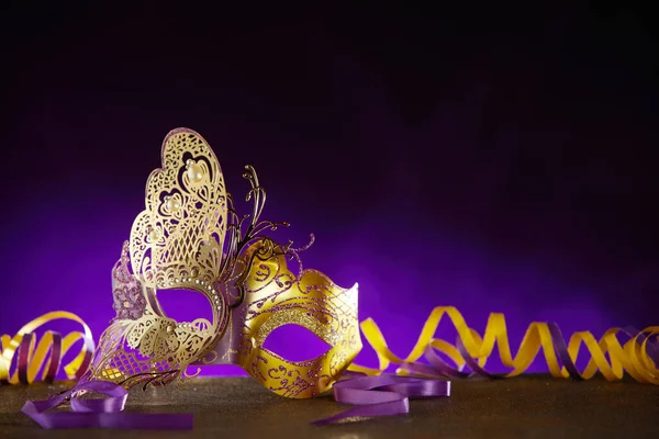 Carnival or Mardi gras background with a decorative face mask in the shape of a gold butterfly with twirled gold streamer in dramatic purple light with copy space