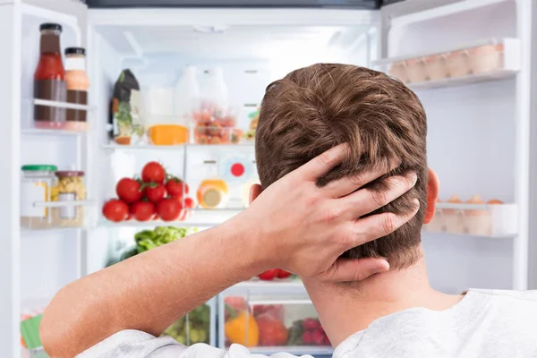 Közelkép Egy Zavarodott Férfiról Aki Ételt Néz Egy Nyitott Hűtőszekrényben — Stock Fotó