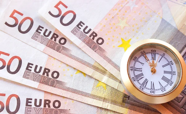 stock image Euro banknotes like background and at the front are clocks that have five to twelve time. Highest time for action.