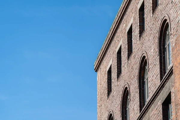 Top corner of brick building facade with arched windows, viewed from low angle against clear blue sky.
