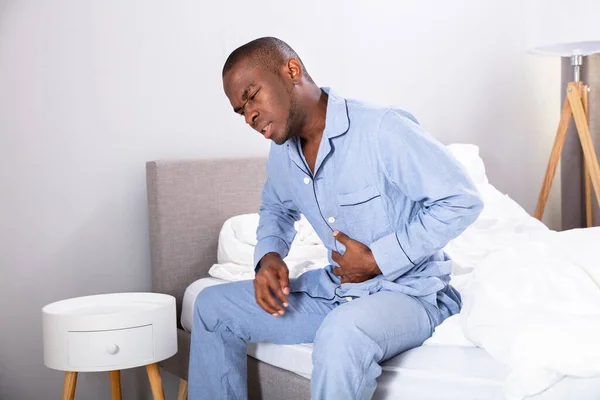 Afrikaner Sitzt Auf Bett Und Leidet Unter Bauchschmerzen — Stockfoto