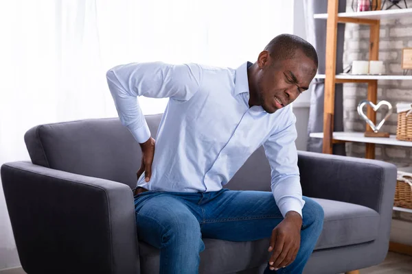 Junger Afrikaner Sitzt Mit Rückenschmerzen Auf Sofa — Stockfoto