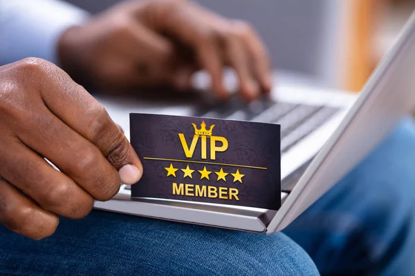 Close-up Of A Man\'s Hand Holding VIP Member Card While Using Laptop