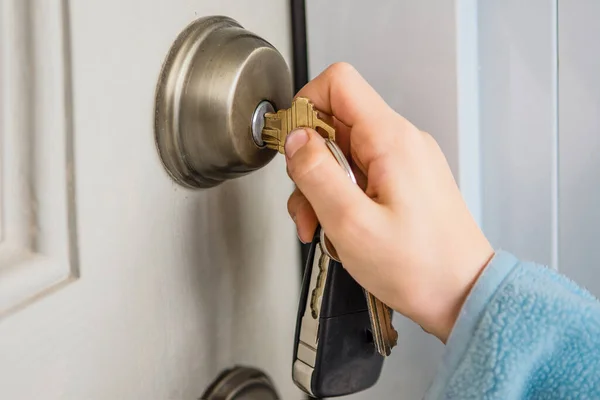 The hand turns the key in the door lock of the front door to the house