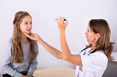 Mature Female Doctor Examining Girl Patient's Eye In Clinic clipart