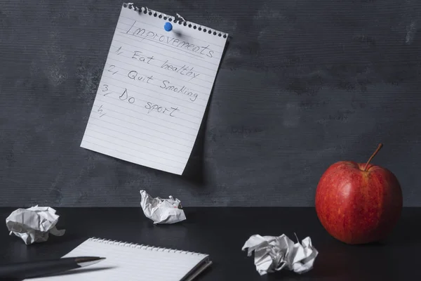 空のスパイラルノートブック 黒い机の上の紙と赤いリンゴ 壁に固定された改善リストのページ ライフスタイルの変化目標 — ストック写真