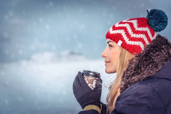 모자를 뜨거운 머그를 눈내리는 즐기며 겨울에 밖에서 즐겁게 아름다운 여인의 — 스톡 사진