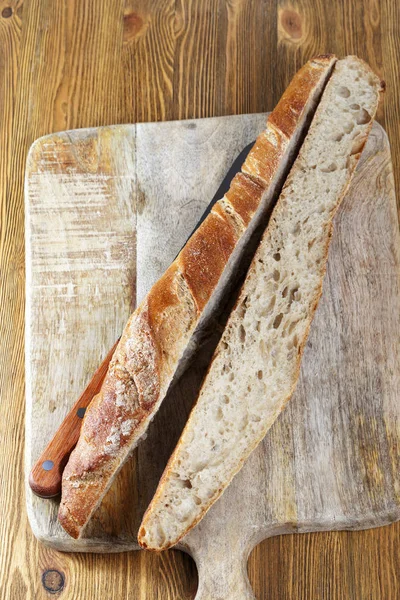 用小刀沿着一块脆而新鲜的面包切在一块木板上 — 图库照片