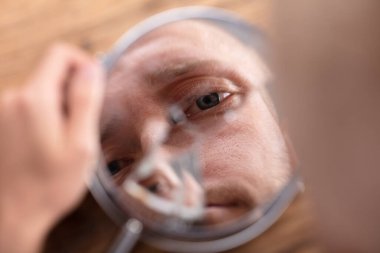 Close-up Of A Man's Face In Broken Mirror Over Wooden Desk clipart