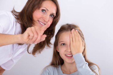Smiling Female Optometrist Assisting Girl While Checking Eyesight In Clinic clipart