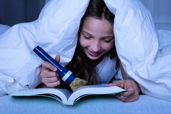 Дівчина Під Білою Ковдрою Використовуючи Ліхтарик Під Час Читання Книги — стокове фото