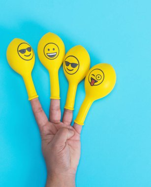 yellow balloons with faces placed on the fingers of the hand on a blue background clipart