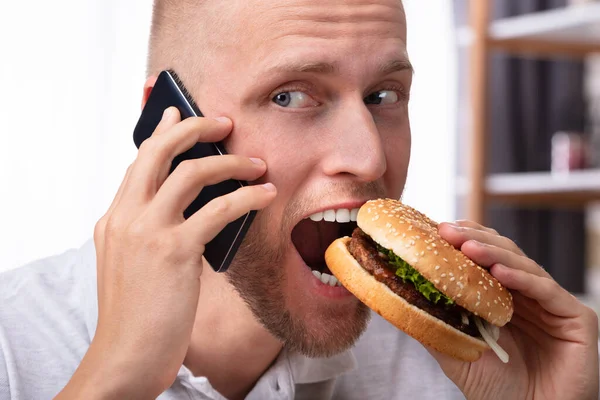 Ritratto Giovane Uomo Che Parla Sul Cellulare Mentre Mangia Hamburger — Foto Stock