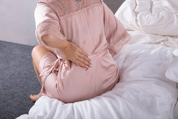 stock image Rear View Of A Woman Sitting On Bed Suffering From Back Pain In Bedroom