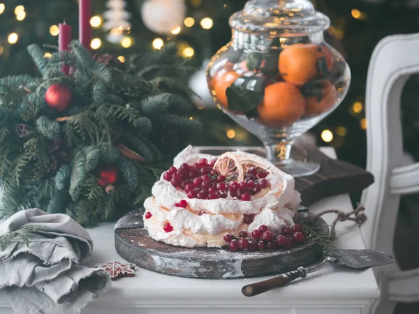 Meringue cake Pavlova with fresh red currant and whipped cream on fir christmas tree background. Mood and Atmospheric photo for winter holidays. New Zealand Australian dessert pavlova. Copy space