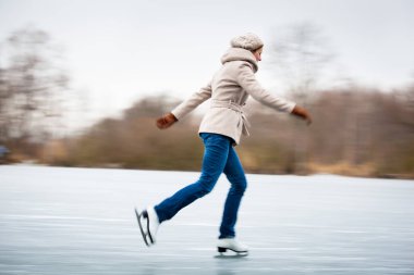 Young woman ice skating outdoors on a pond on a freezing winter day clipart