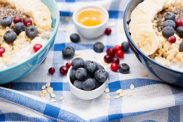 Healthy fitness breakfast: oatmeal with bananas, blueberries and cranberries, chia seeds and yogurt on blue and white towel