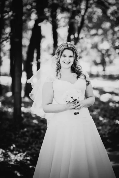在夏日公园的特写中 黑色的白色摄影时尚美丽而快乐的新娘手持一束鲜花 背景是树木 — 图库照片