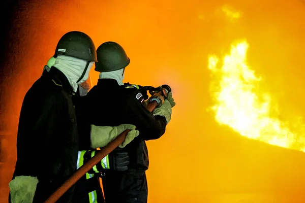 ドイツの消防の訓練が消防士 煙が付いている火に水を噴霧の火の保護スーツで消防士 トレーニング中に攻撃を火災消防士の戦い — ストック写真