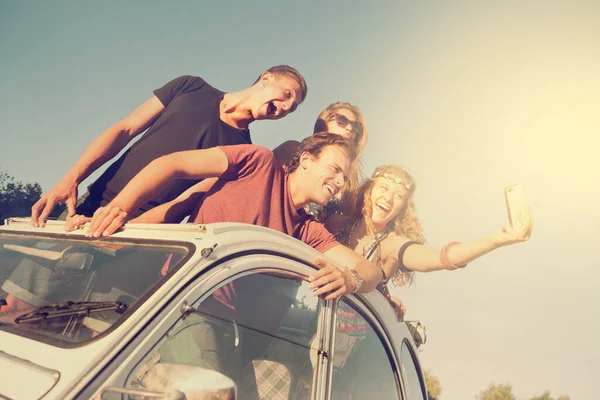Group of happy people taking a selfie in a car at sunset in summer.