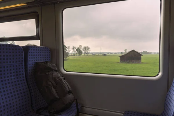 在靠窗的火车座位上背包 在窗口上可以看到巴伐利亚风景的内部列车 — 图库照片