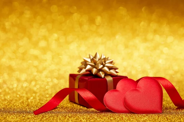 コピースペース付きのきらびやかな金の背景に2つの装飾的な心とギフトボックス バレンタインデーカード ロマンチックなグリーティングカード 結婚式の招待状のデザイン要素 — ストック写真