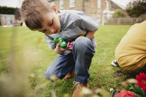 イースター卵上の少年は 友人と狩り 家の裏庭でチョコレートのイースターの卵を探しています — ストック写真