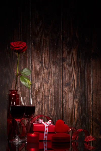 Still life with rose, red heart, gift box and two glasses with wine on a wooden background. Valentine's Day card with copy space. Design element for romantic greeting card, wedding invitation,