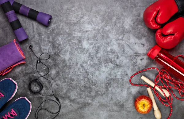 Fitness still life with dumbbells, rope, boxing gloves, sneakers, bottle for water and  smart bracelet on grey background. Top view with copy space. Fitness, sport and healthy lifestyle concept.