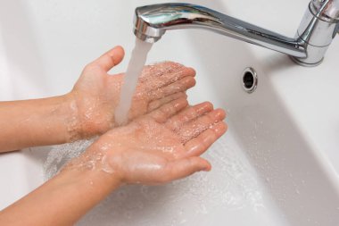 Children's hands under a strong stream of water from the mixer in the bathroom clipart