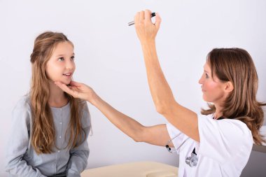 Mature Female Doctor Examining Girl Patient's Eye In Clinic clipart