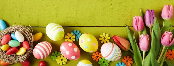 Baner Wielkanocny Kolorowymi Jajkami Cukierkami Kwiatami Tulipanów Jasnozielonym Drewnianym Tle — Zdjęcie stockowe
