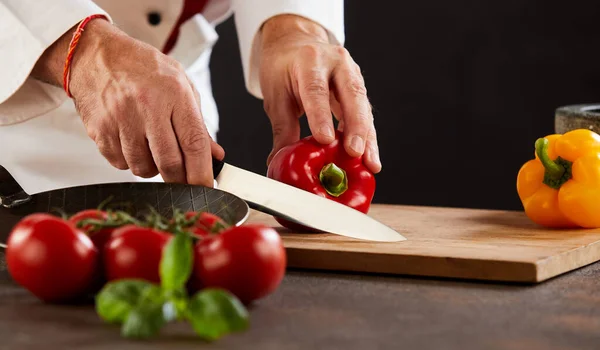 男厨师用一把锋利的大刀在木板上切新鲜辣椒或甜辣椒 — 图库照片