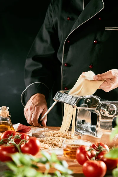 手作りのカッターで手作りパスタ麺を作るイタリア人シェフが生地をガイドしながらハンドルを回す — ストック写真