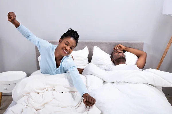 Happy African Woman Stretching While Her Husband Lying On Bed In Bedroom