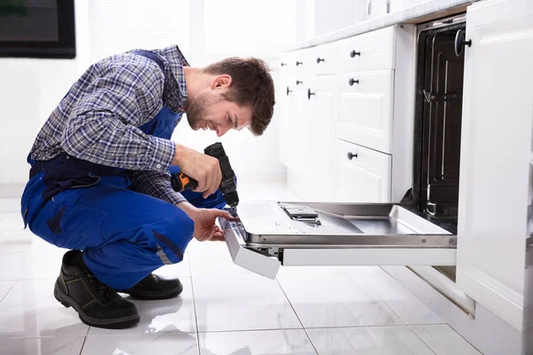 Jovem Reparador Fixando Máquina Lavar Louça Com Broca Elétrica Cozinha — Fotografia de Stock