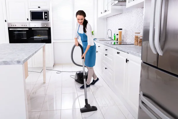 Young Female Janitor In Uniform Cleaning Kitchen Floor With Vacuum Floor