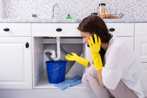 Sad Young Woman Calling Plumber Front Water Leaking Sink Pipe — Stock Photo, Image