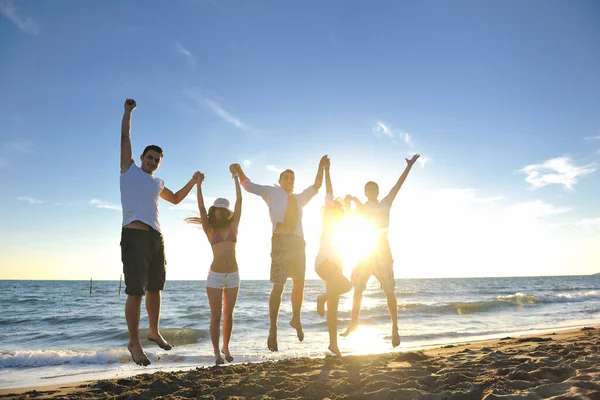 幸せな若い友人グループは楽しい時間を過ごし 夕日のビーチでジャンプして走りながらお祝いします — ストック写真