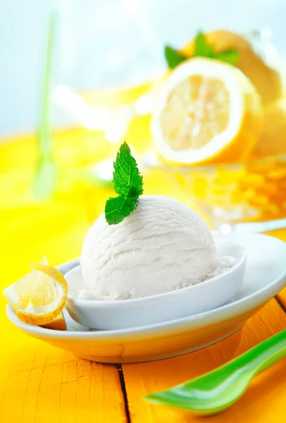 Serving of refreshingly sour lemon sorbet icecream with mint leaves served on a tilted yellow table top