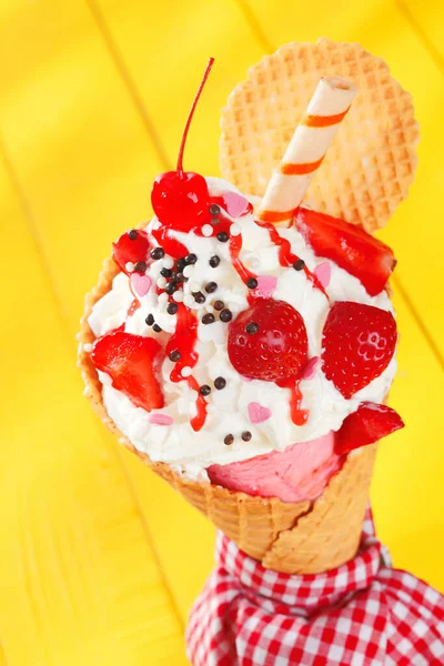 鮮やかな黄色を背景に 熟した赤いイチゴとスパイラルウェーハビスケットが添えられたカラフルなパーティーアイスクリームコーン — ストック写真