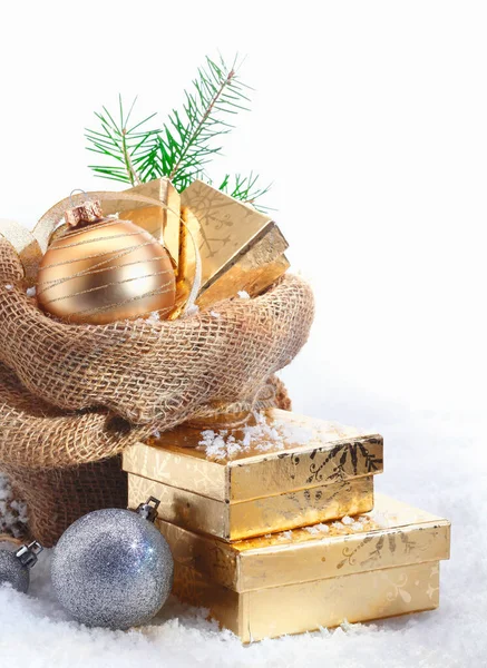 Rustic Christmas gift background with decorative baubles and golden gifts spilling out of a simple hessian sack onto the snowcovered ground with copyspace
