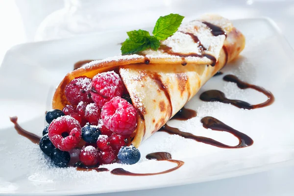 Fresh fried golden pancake filled with an assortment of berries drizzled with chocolate and garnished with mint